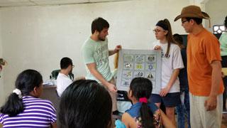 three college students at front of classroom of middle school students in Panama holding chart and doing demonstration